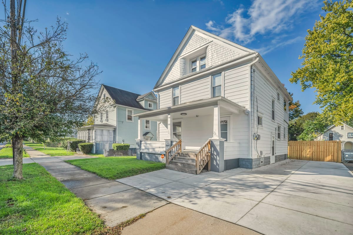 A white two-story house with a covered front porch and a concrete drive.